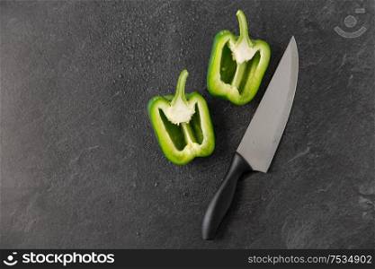 vegetable, food and culinary concept - close up of cut green pepper and kitchen knife on slate stone background. green pepper and kitchen knife on slate background