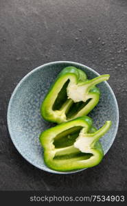 vegetable, food and culinary concept - close up of cut green pepper in bowl on slate stone background. cut green pepper in bowl on slate stone background