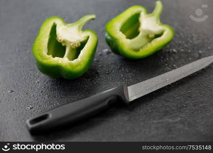 vegetable, food and culinary concept - close up of cut green pepper and kitchen knife on slate stone background. green pepper and kitchen knife on slate background