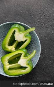 vegetable, food and culinary concept - close up of cut green pepper in bowl on slate stone background. cut green pepper in bowl on slate stone background