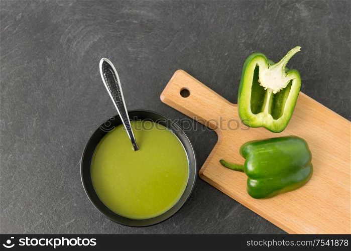 vegetable, food and culinary concept - close up of cut green peppers in ceramic bowl and paprika cream soup on slate stone background. green pepper or paprika cream soup in bowl