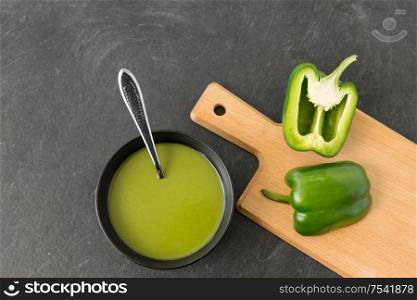 vegetable, food and culinary concept - close up of cut green peppers in ceramic bowl and paprika cream soup on slate stone background. green pepper or paprika cream soup in bowl
