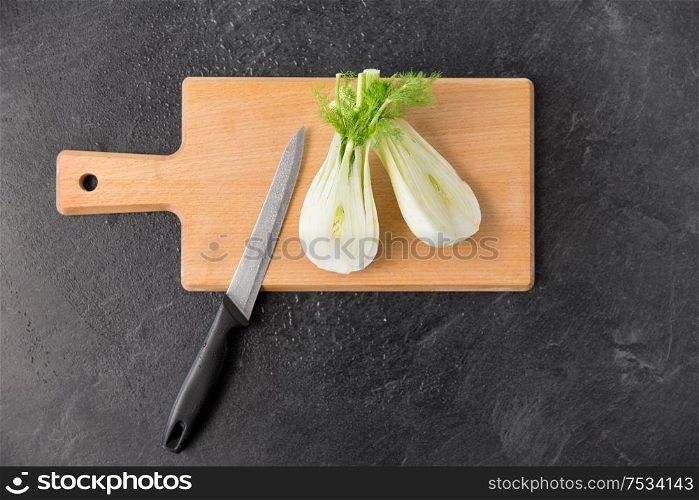 vegetable, food and culinary concept - close up of fennel and kitchen knife on wooden cutting board on slate stone background. fennel and kitchen knife on wooden cutting board