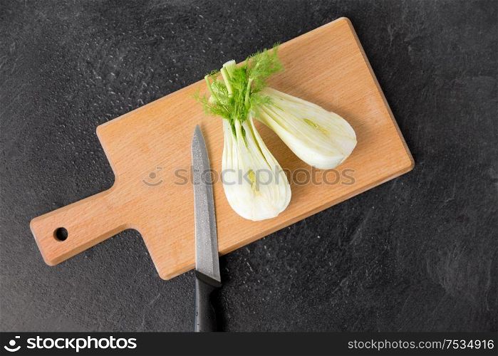 vegetable, food and culinary concept - close up of fennel and kitchen knife on wooden cutting board on slate stone background. fennel and kitchen knife on wooden cutting board