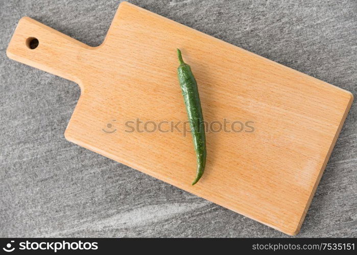 vegetable, food and culinary concept - close up of green chili pepper on wooden cutting board on slate stone background. green chili pepper on wooden cutting board
