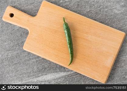 vegetable, food and culinary concept - close up of green chili pepper on wooden cutting board on slate stone background. green chili pepper on wooden cutting board