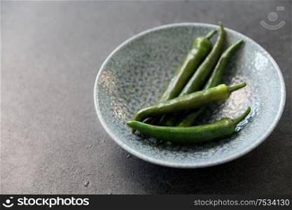 vegetable, food and culinary concept - close up of green chili peppers in ceramic bowl on slate stone background. close up of green chili peppers in bowl