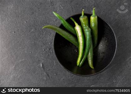 vegetable, food and culinary concept - close up of green chili peppers in ceramic bowl on slate stone background. close up of green chili peppers in bowl