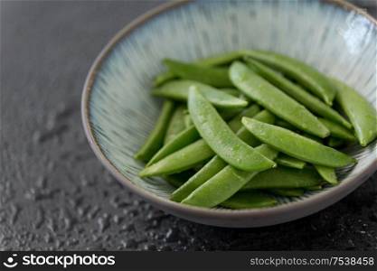 vegetable, food and culinary concept - close up of peas in bowl on wet slate stone background. peas in bowl on wet slate stone background