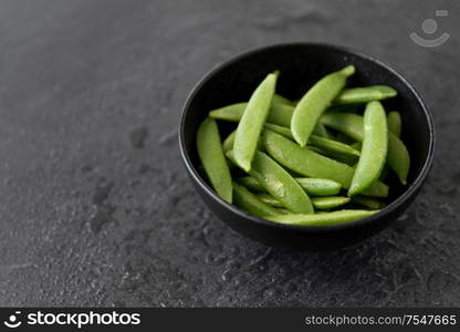 vegetable, food and culinary concept - close up of peas in bowl on wet slate stone background. peas in bowl on wet slate stone background