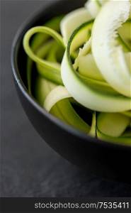 vegetable, food and culinary concept - close up of peeled or sliced zucchini in ceramic bowl on slate stone background. peeled or sliced zucchini in ceramic bowl