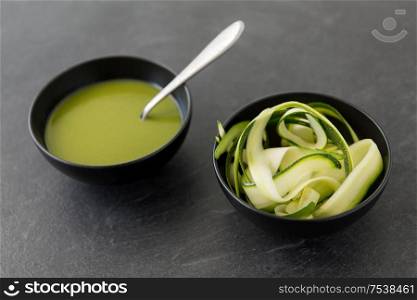 vegetable, food and culinary concept - close up of peeled or sliced zucchini and cream soup in ceramic bowl on slate stone background. peeled or sliced zucchini and cream soup in bowl