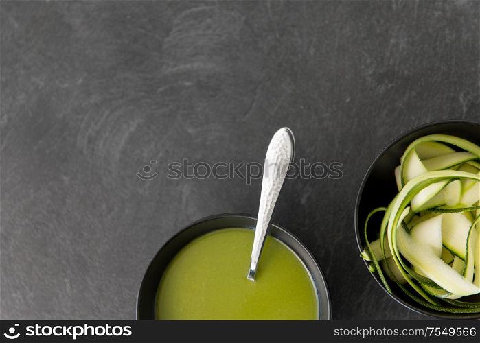 vegetable, food and culinary concept - close up of peeled or sliced zucchini and cream soup in ceramic bowl on slate stone background. peeled or sliced zucchini and cream soup in bowl