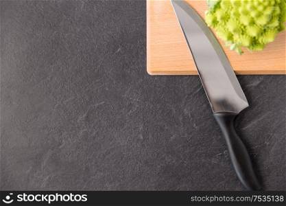 vegetable, food and culinary concept - close up of romanesco broccoli and kitchen knife on wooden cutting board on slate stone background. romanesco broccoli and knife on cutting board