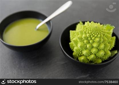 vegetable, food and culinary concept - close up of romanesco broccoli cream soup in ceramic bowl on slate stone background. close up of romanesco broccoli cream soup in bowl