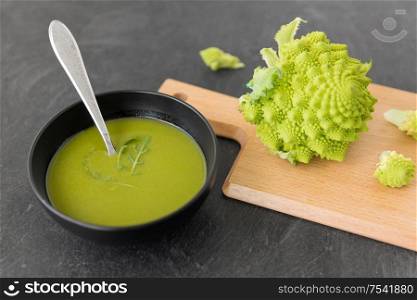 vegetable, food and culinary concept - close up of romanesco broccoli cream soup in ceramic bowl on slate stone background. close up of romanesco broccoli cream soup in bowl