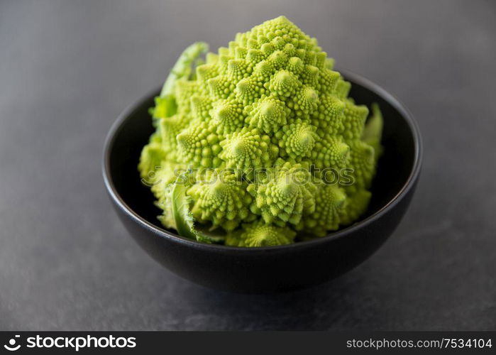 vegetable, food and culinary concept - close up of romanesco broccoli in ceramic bowl on slate stone background. close up of romanesco broccoli in bowl