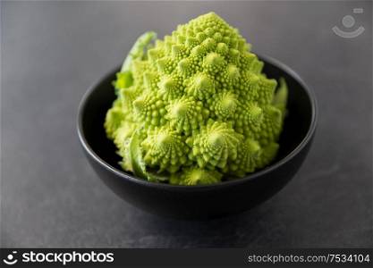 vegetable, food and culinary concept - close up of romanesco broccoli in ceramic bowl on slate stone background. close up of romanesco broccoli in bowl