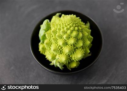 vegetable, food and culinary concept - close up of romanesco broccoli in ceramic bowl on slate stone background. close up of romanesco broccoli in bowl