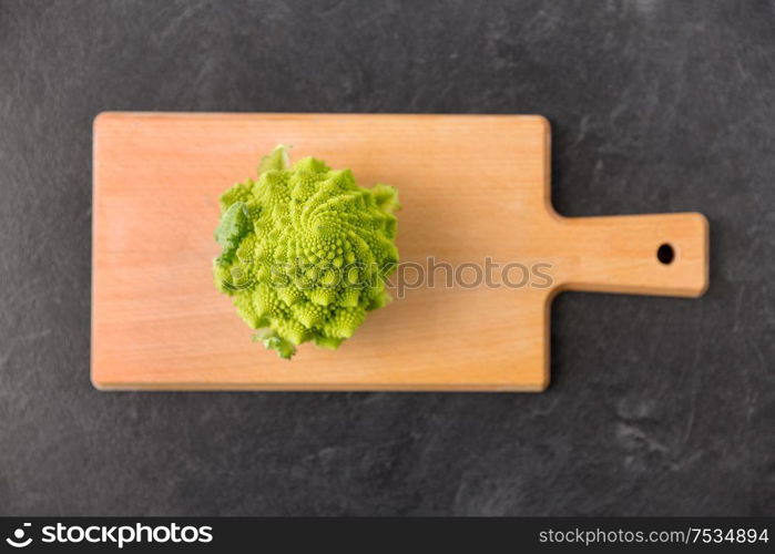 vegetable, food and culinary concept - close up of romanesco broccoli on wooden cutting board on slate stone background. romanesco broccoli on wooden cutting board