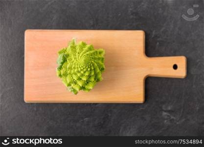 vegetable, food and culinary concept - close up of romanesco broccoli on wooden cutting board on slate stone background. romanesco broccoli on wooden cutting board