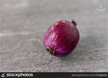 vegetable, food and culinary concept - close up of wet red onion on slate stone background. close up of red onion on slate stone background