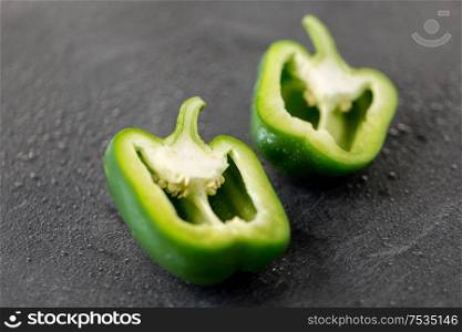 vegetable, food and culinary concept - cut green pepper on slate stone background. cut green pepper on slate stone background