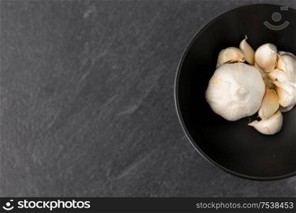 vegetable, food and culinary concept - garlic in bowl on slate stone background. garlic in bowl on slate stone background