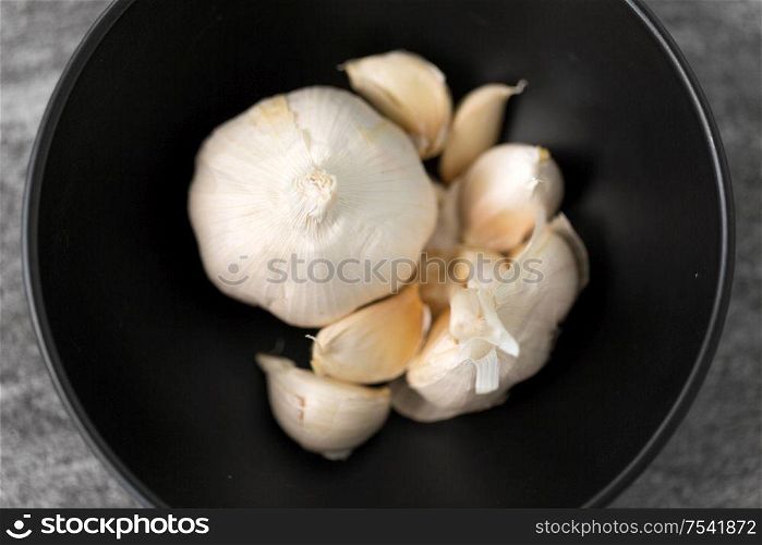 vegetable, food and culinary concept - garlic in bowl on slate stone background. garlic in bowl on slate stone background