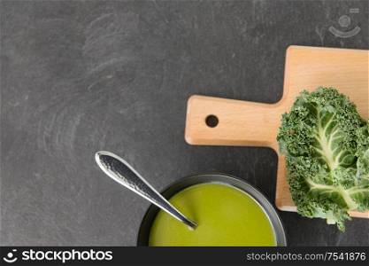 vegetable, food and culinary concept - kale cabbage cream soup in ceramic bowl with spoon on slate stone background. kale cabbage cream soup in bowl with spoon