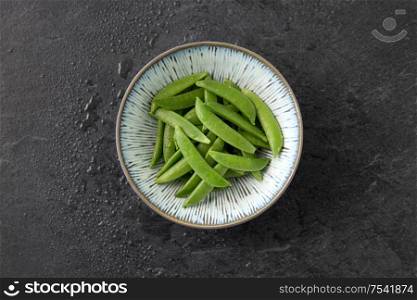 vegetable, food and culinary concept - peas in bowl on wet slate stone background. peas in bowl on wet slate stone background