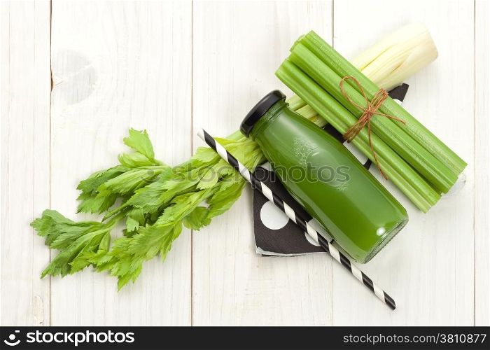 Vegetable juice in bottle with celery stalk on white wood background