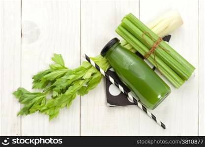 Vegetable juice in bottle with celery stalk on white wood background
