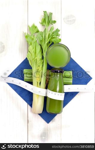 Vegetable juice with fresh celery and measuring tape on white wood