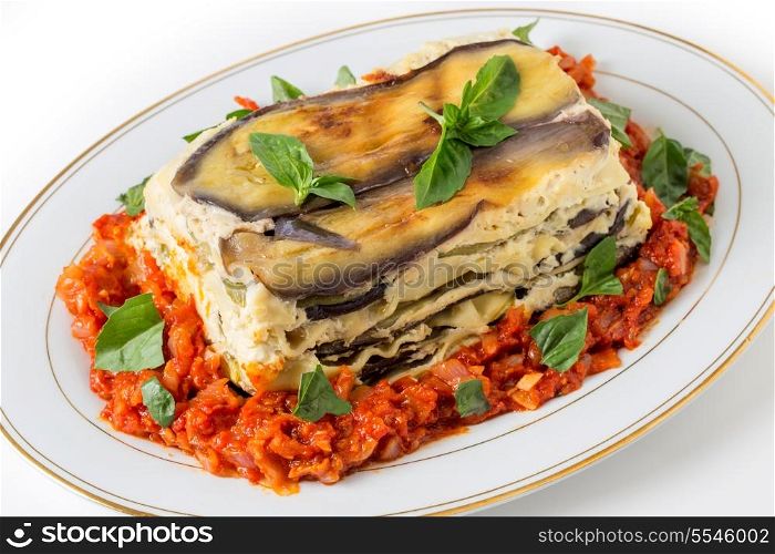Vegetable lasagne, made with courgettes and eggplants (zucchini and aubergines), pasta sheets and bechamel sauce, served with a tomato and onion sauce and a basil garnish.