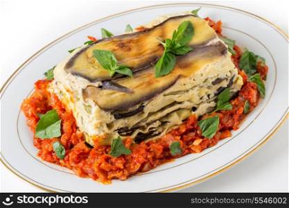Vegetable lasagne, made with courgettes and eggplants (zucchini and aubergines), pasta sheets and bechamel sauce, served with a tomato and onion sauce and a basil garnish.