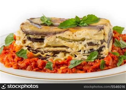 Vegetable lasagne, made with courgettes and eggplants (zucchini and aubergines), pasta sheets and bechamel sauce, served with a tomato and onion sauce and a basil garnish, side view