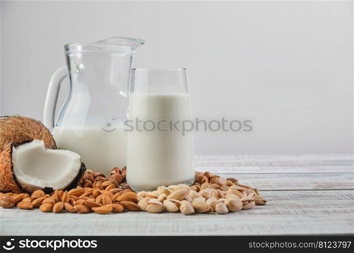Vegetable milk in a glass and jug on a wooden background. Vegetable milk from different ingredients  coconut, hazelnuts, cashews, pistachios, almonds. Healthy Eating 