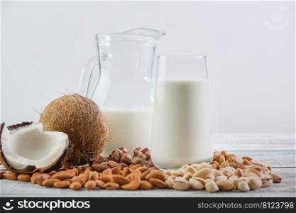 Vegetable milk in a glass and jug on a wooden background. Vegetable milk from different ingredients  coconut, hazelnuts, cashews, pistachios, almonds. Healthy Eating 