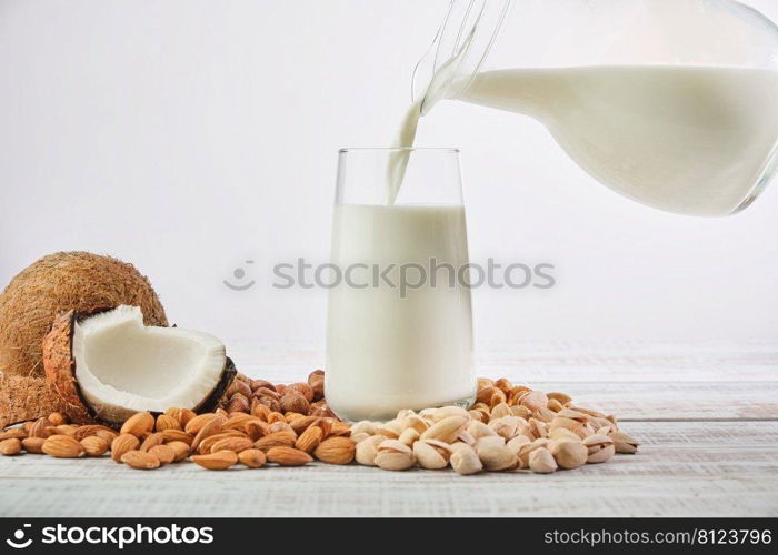 Vegetable milk is poured into a glass from a jug on a wooden background. Vegetable milk from different ingredients  coconut, hazelnuts, cashews, pistachios, almonds. Healthy Eating 