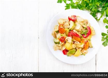 Vegetable ragout with zucchini, cabbage, potatoes, tomatoes and bell peppers in creamy sauce in plate, napkin, parsley and fork on wooden board background from above