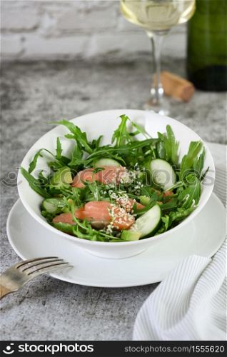 Vegetable salad from arugula, avocado and cucumber pieces with the addition of tender salted salmon, seasoned sesame seeds