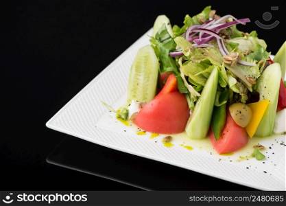 vegetable salad in a square plate on a black background, isolated. dish on black background