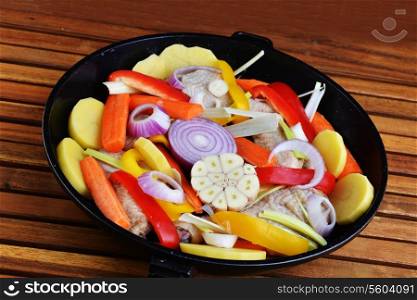 vegetables and chicken in pan on wooden background