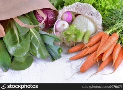 vegetables in a reusable  and paper bags among other  fresh vegetables  on a white table