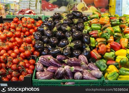 Vegetables in crates in supermarket. Arranged eggplants, peppers and tomatoes.