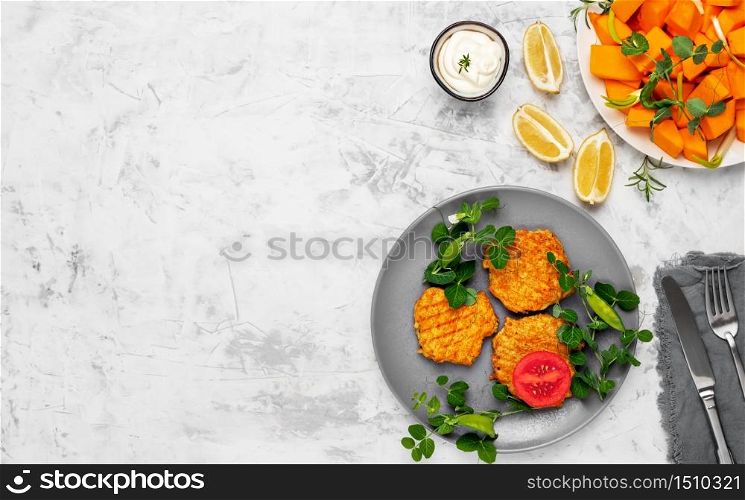 Vegetables patties of pumpkin or cutlets for vegan burgers on a gray plate on a light gray backgraund. Sauce and slices of pumpkin next to a plate. Top view, copy space