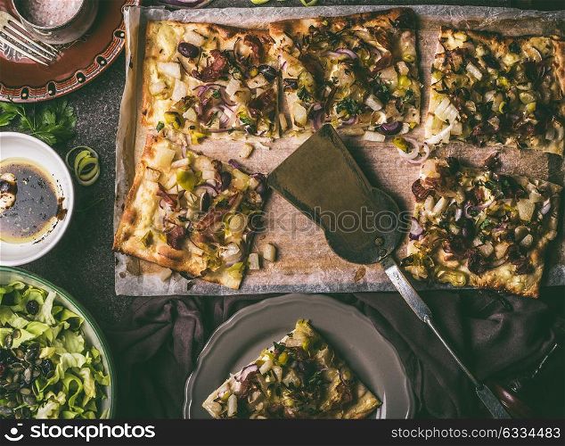 Vegetables tart with leek, served with green salad and dressing on rustic kitchen table background, top view. Tarte flambee - rustic french pie. Vegetarian food