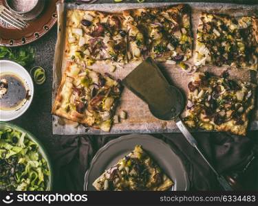 Vegetables tart with leek, served with green salad and dressing on rustic kitchen table background, top view. Tarte flambee - rustic french pie. Vegetarian food