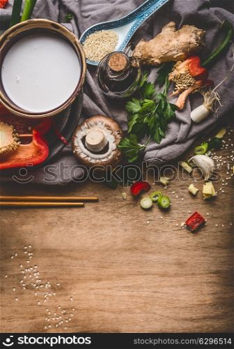 Vegetarian Asian cuisine ingredients with chopped vegetables, coconut milk, seeds, spices and chopsticks on rustic wooden background, top view. Chinese or Thai food cooking